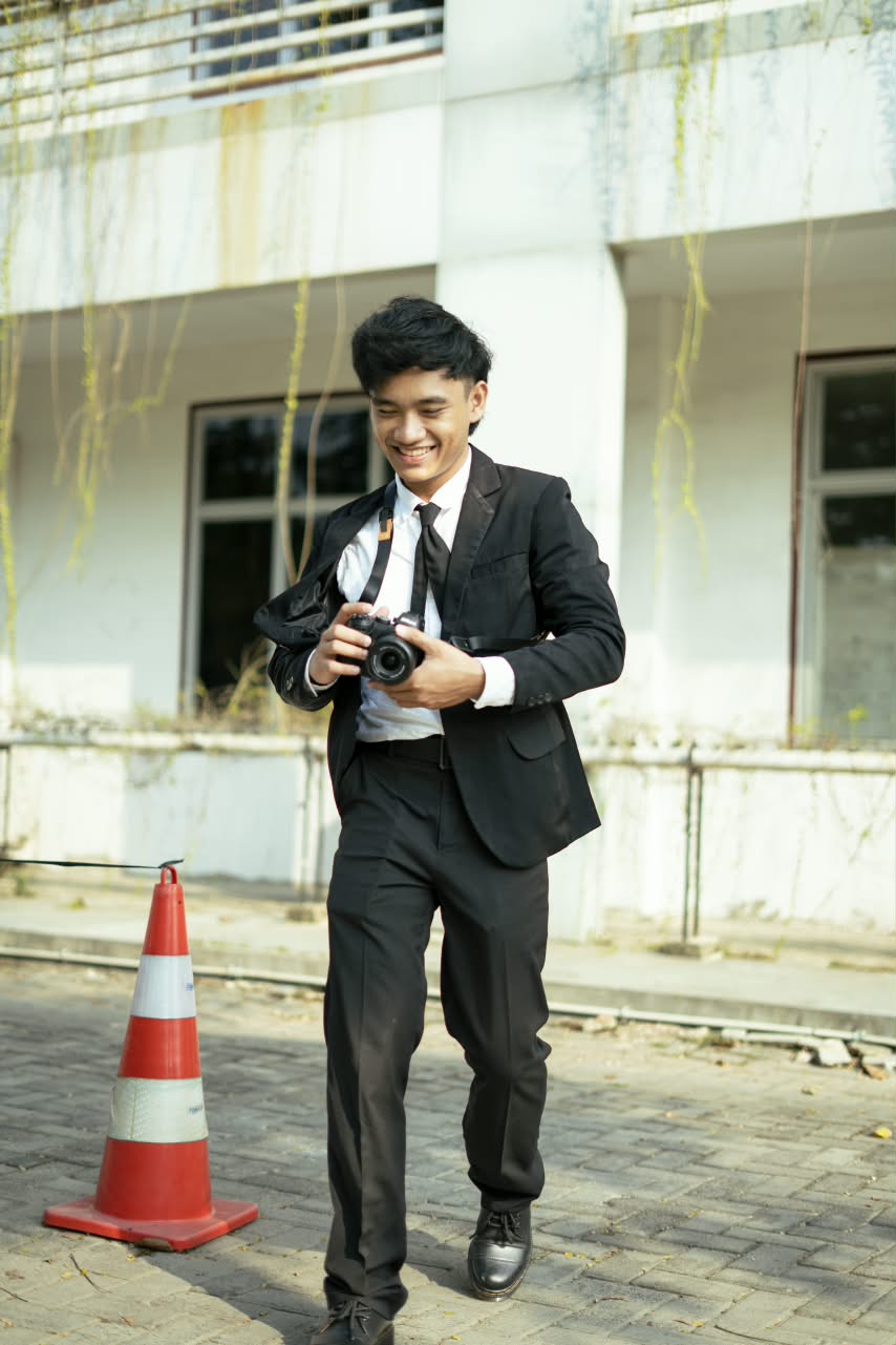 Fotografer mengenakan jas hitam sambil memegang kamera di luar gedung